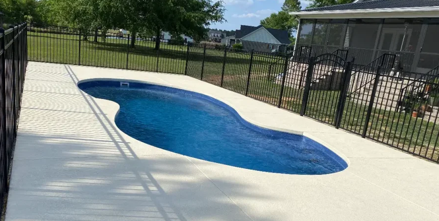 kidney shaped pool in a fenced in backyard area