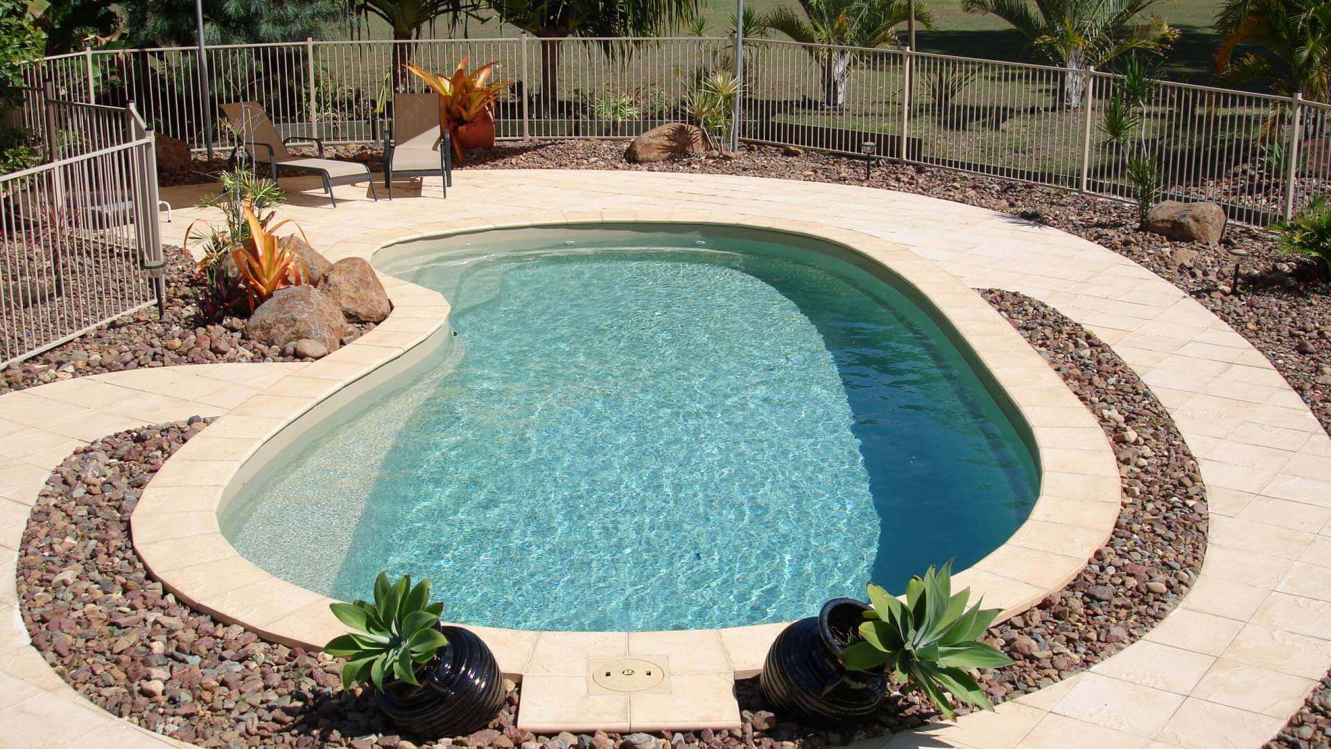 Backyard pool with surrounding plants and chairs.